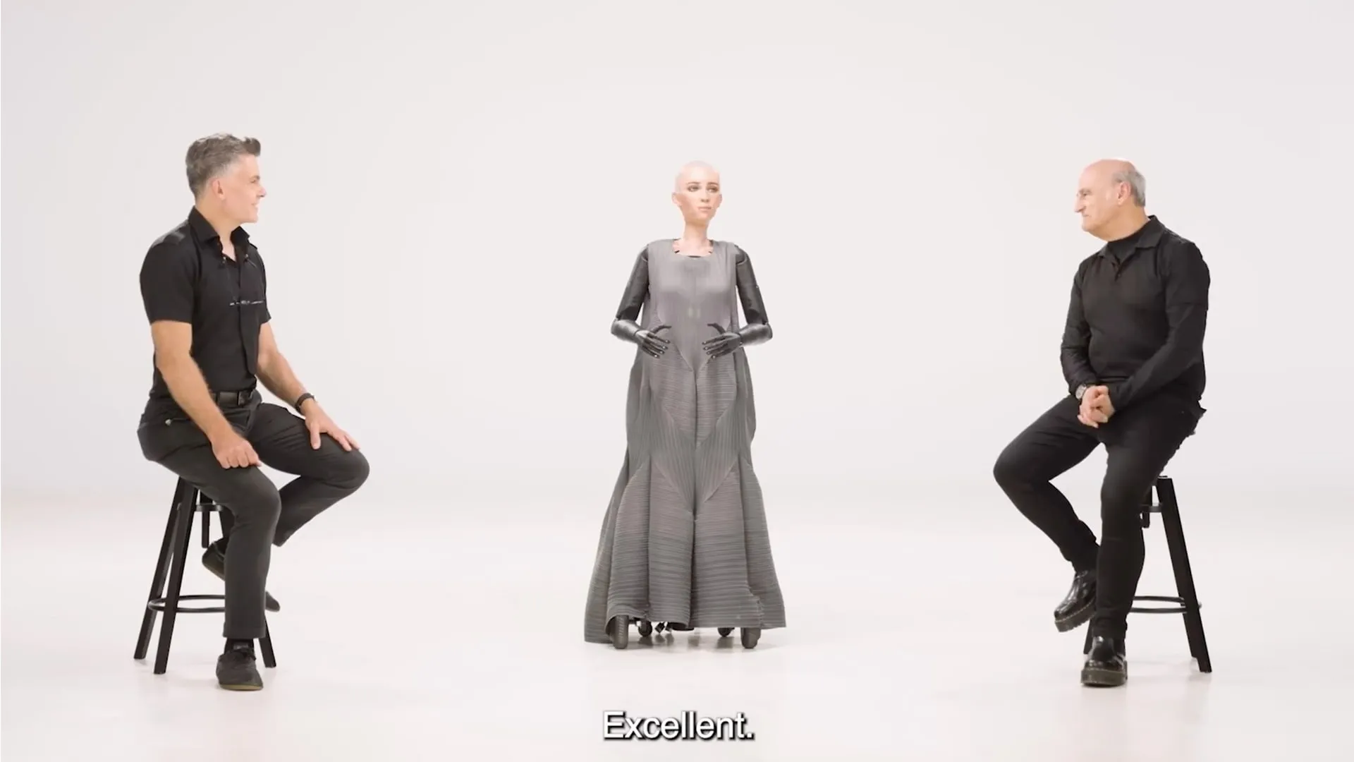 Two hosts seated either side of a humanoid robot