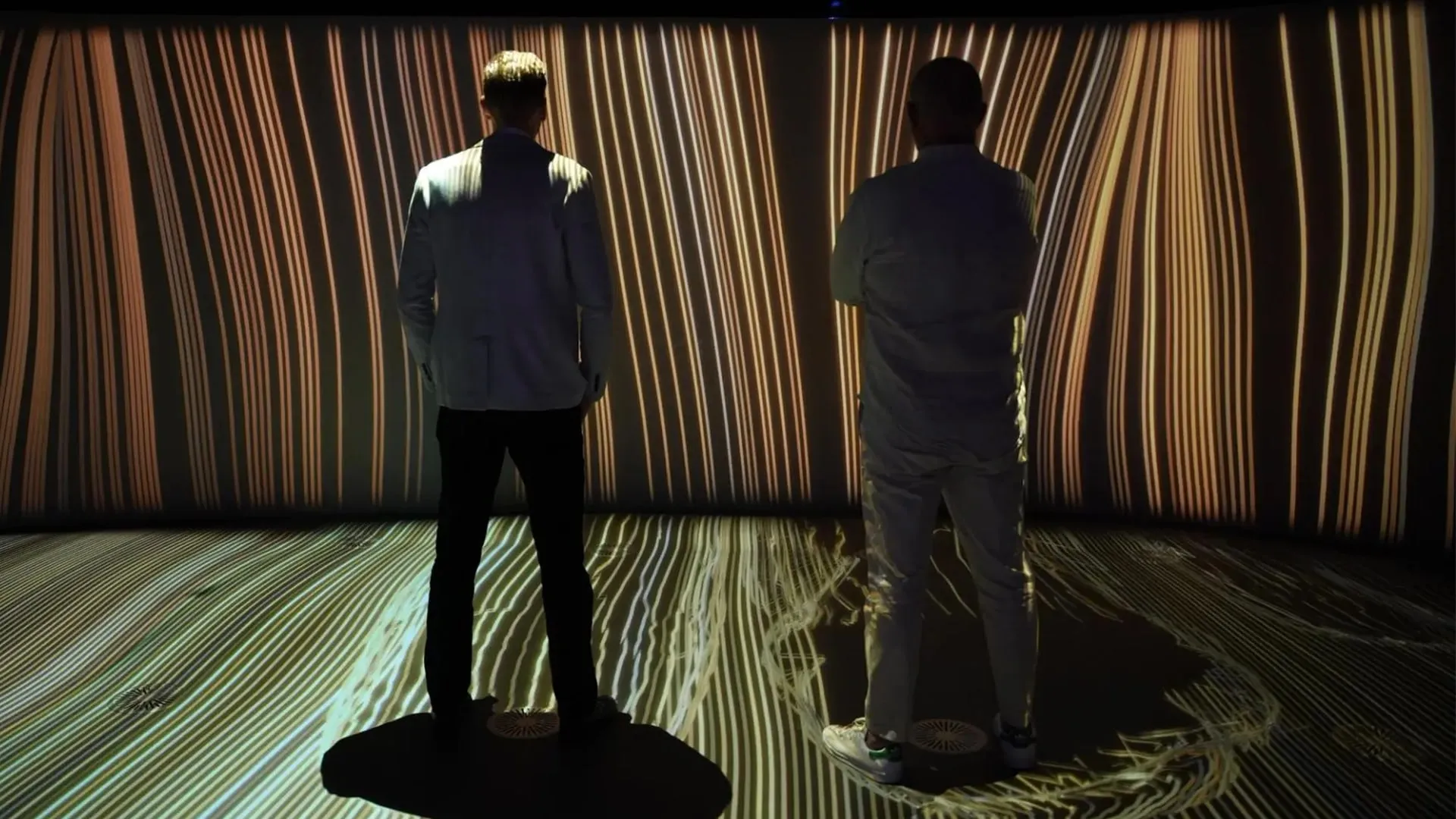Two visitors standing in a room of warm, flowing projections