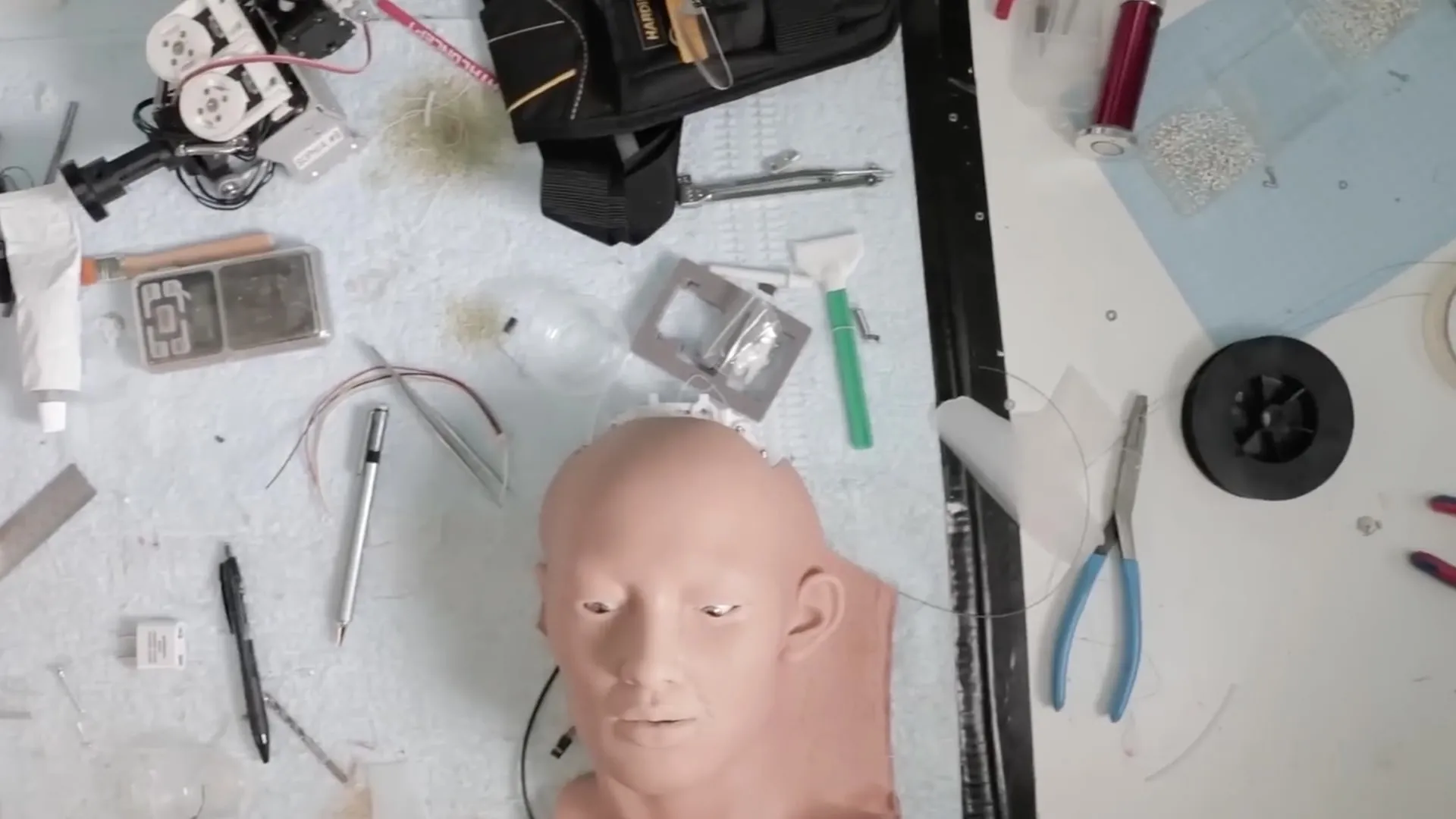 A robot head on a workbench surrounded by tools