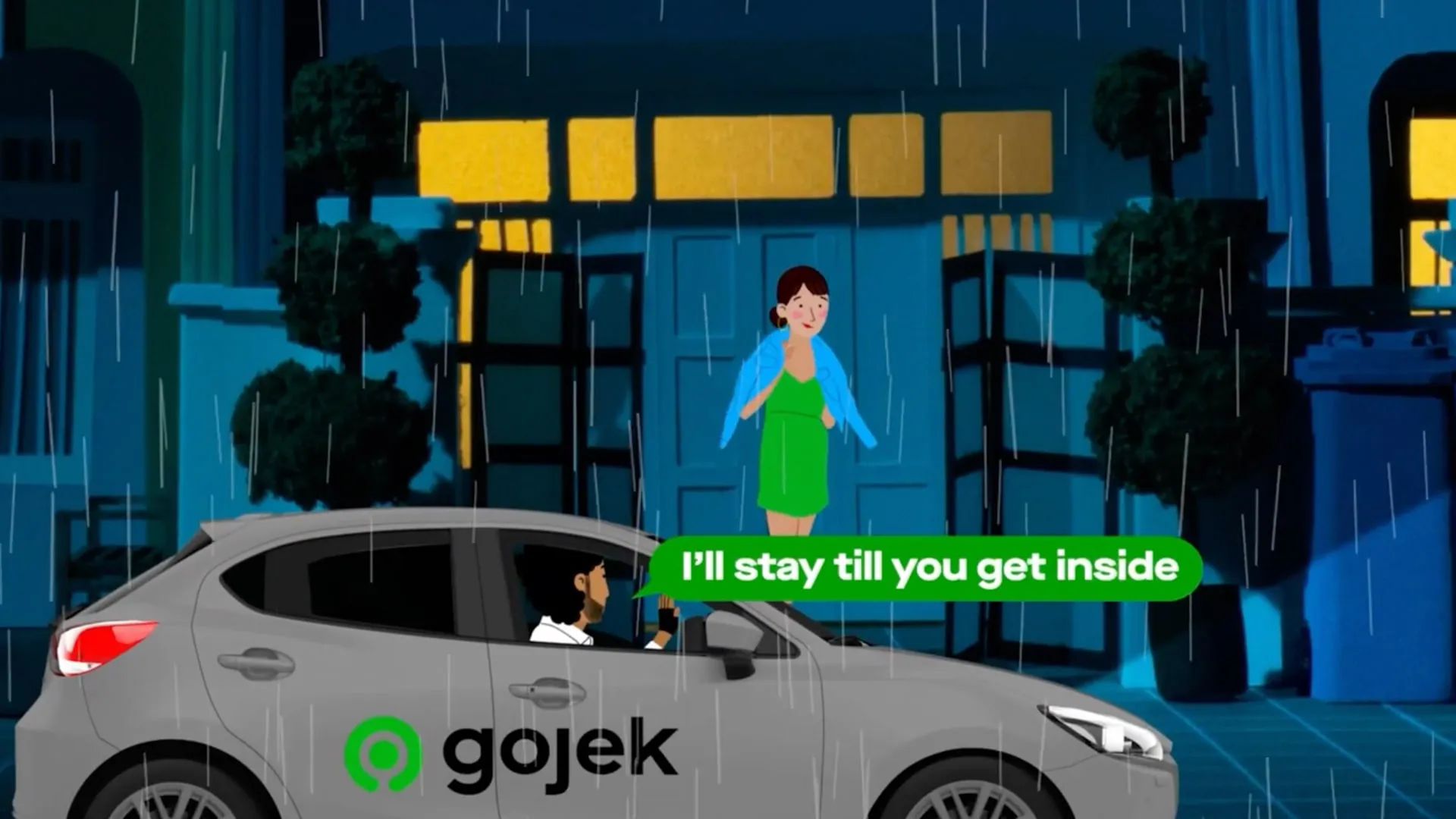 A Gojek car waiting in the rain outside a home at night
