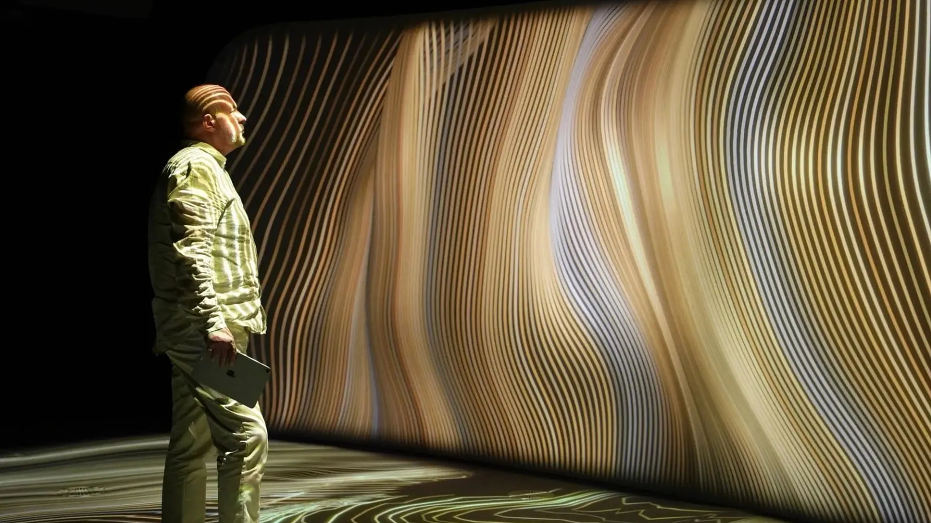 A visitor looking at flowing golden projections on a curved wall