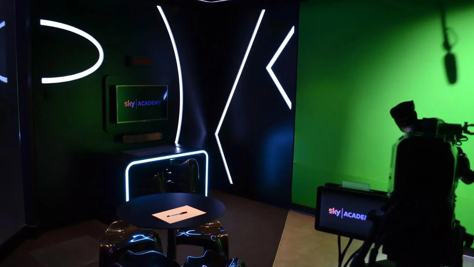 The neon-lit Sky Academy studio set with a broadcast camera