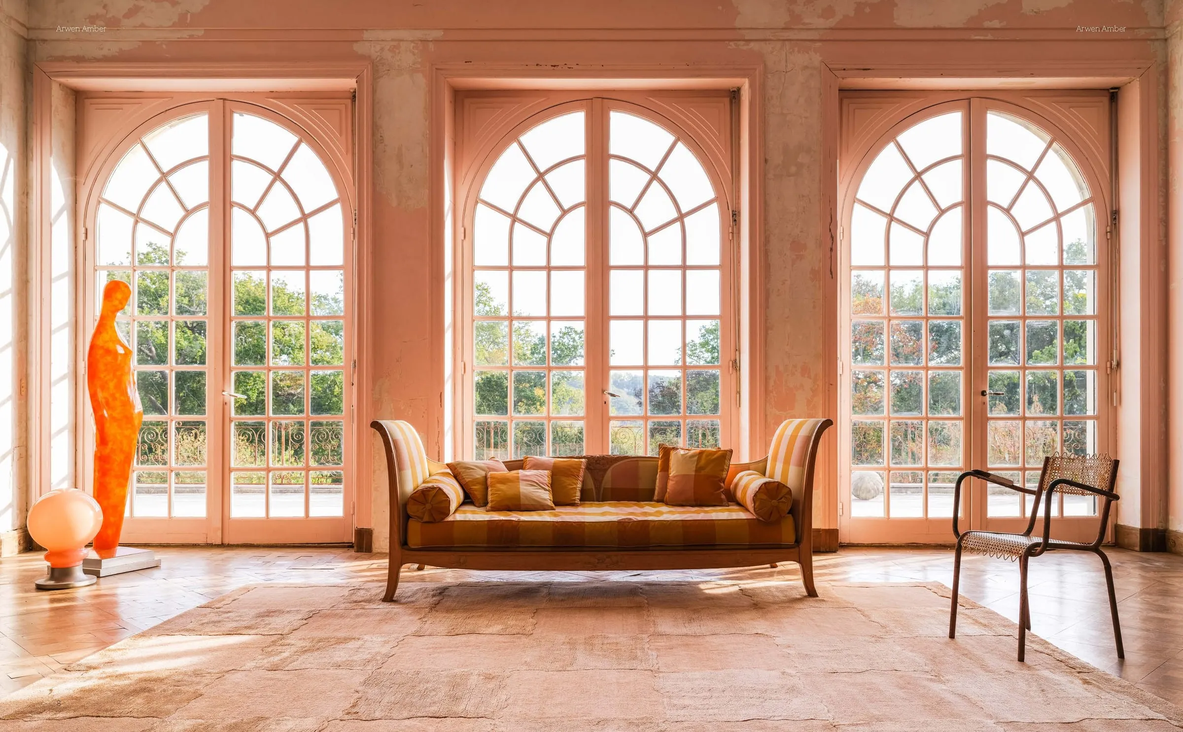 A sunlit room with tall arched windows and a soft-toned rug